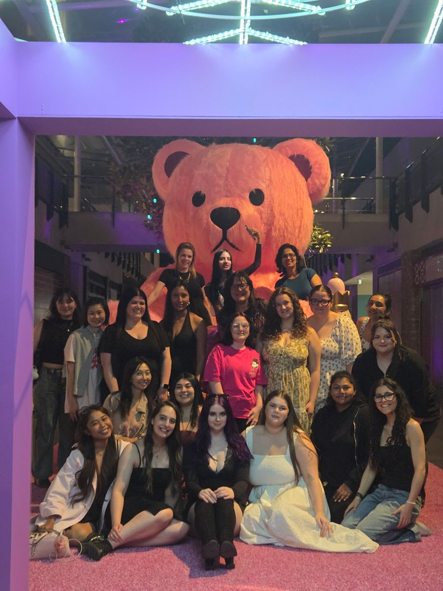 A group of Social Sisters members smiling together in front of a giant pink teddy bear